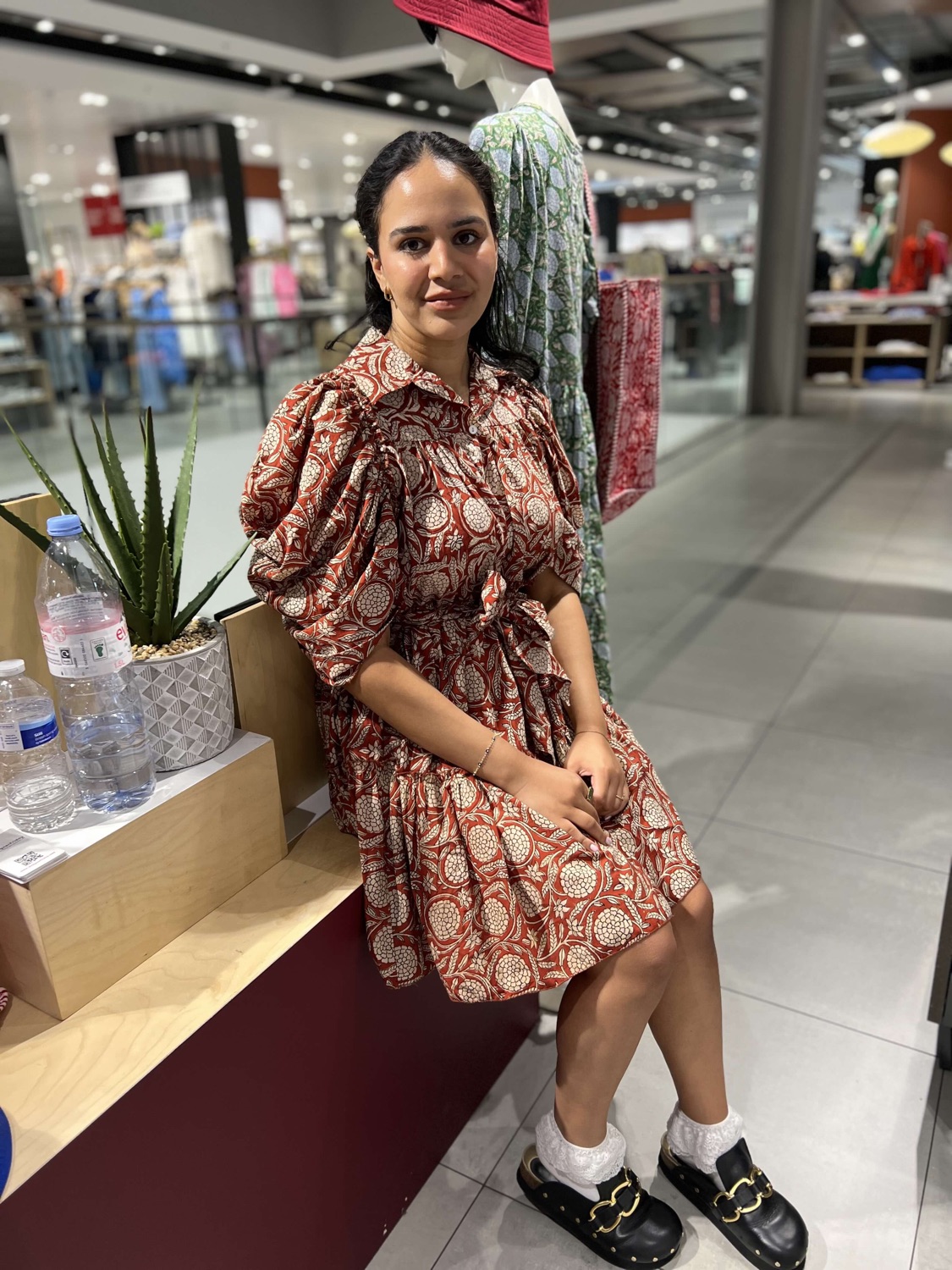 A customer seated wearing a rust and cream block-print DesignerFriday dress beside the popup display.